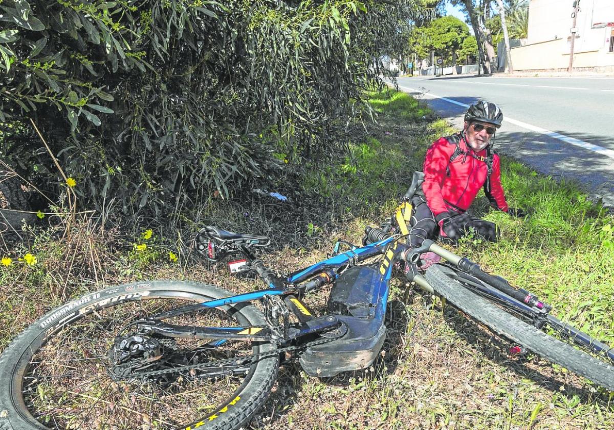 El accidentado sentado en el suelo con su bicicleta en el lugar del suceso días después del choque.