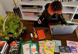 La ilustradora murciana Ana Galvañ rodeada de libros y junto a su libreta roja de bocetos, trabajando con su ordenador y tableta gráfica.