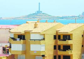 Pisos con cartel de venta o alquiler en un bloque de La Manga con el faro de Cabo de Palos al fondo.