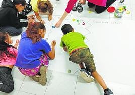 Escolares de Lobosillo, de entre 6 y 12 años, preparan un mural sobre ecosistemas junto a la monitora contratada.