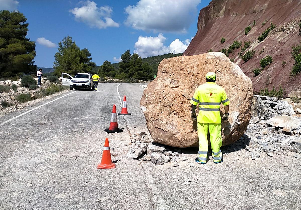 Un operario, junto a una enorme roca caída sobre la carretera.