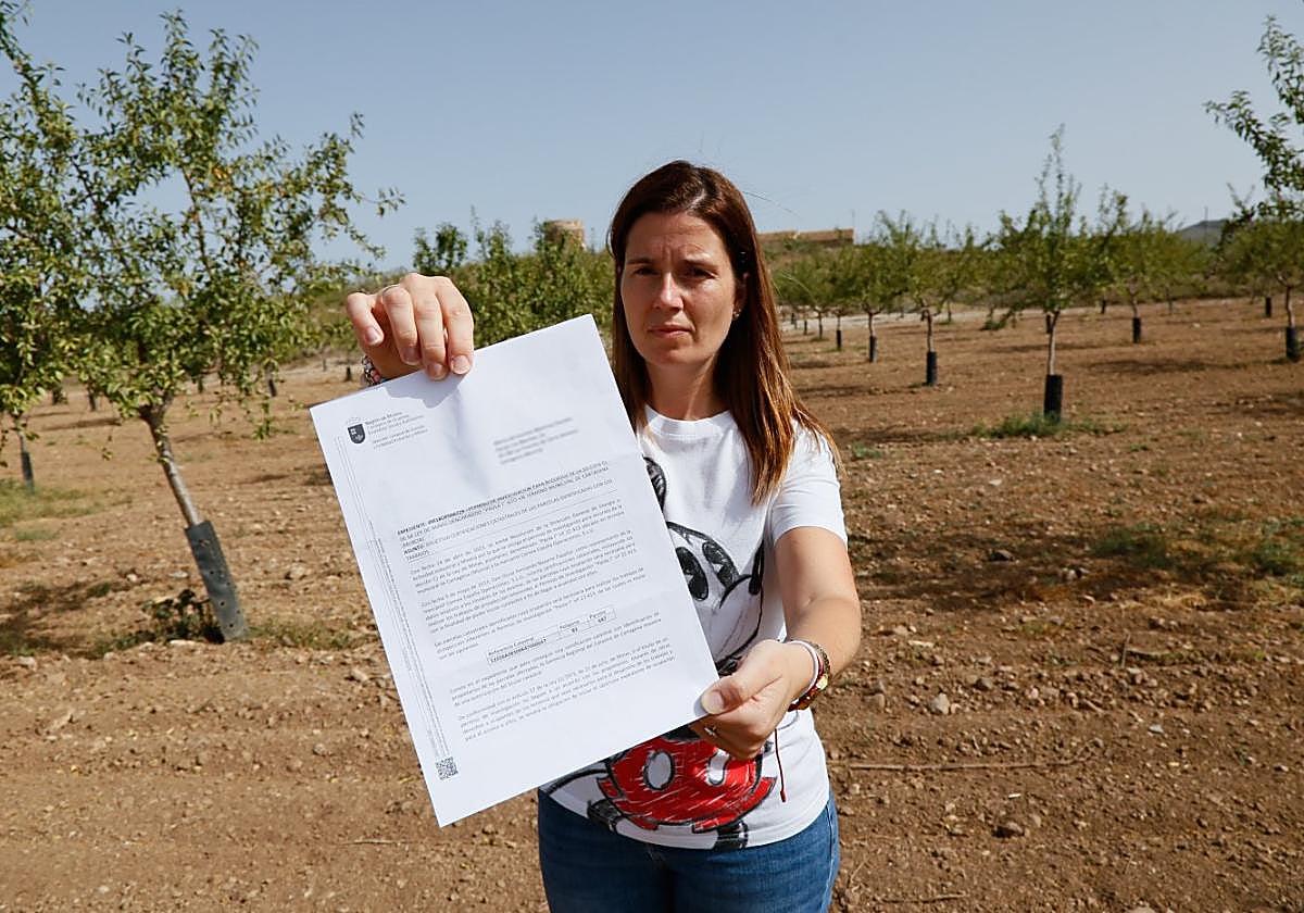 María del Carmen Martínez enseña la carta que recibió de la Carm en su finca de los Puertos de Santa Bárbara con el molino al fondo.