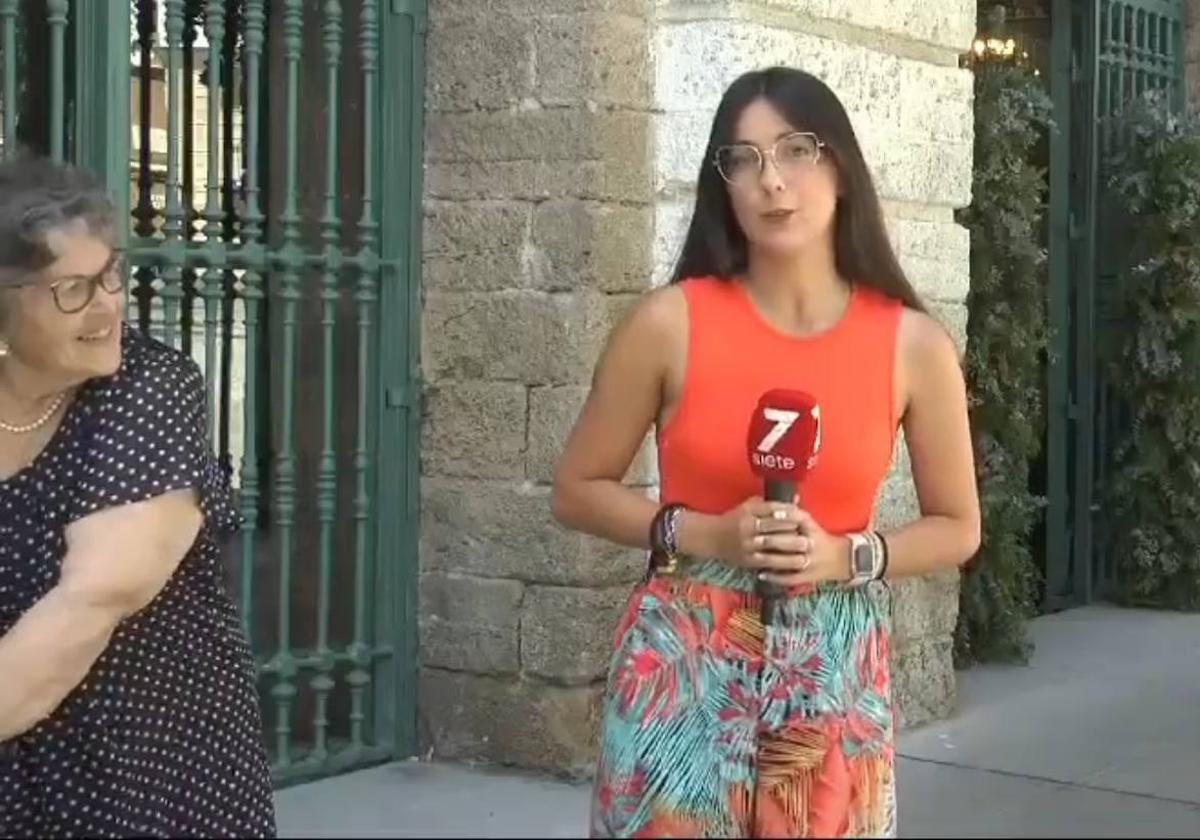 Una mujer observa a una periodista mientras realiza un directo en Cádiz.