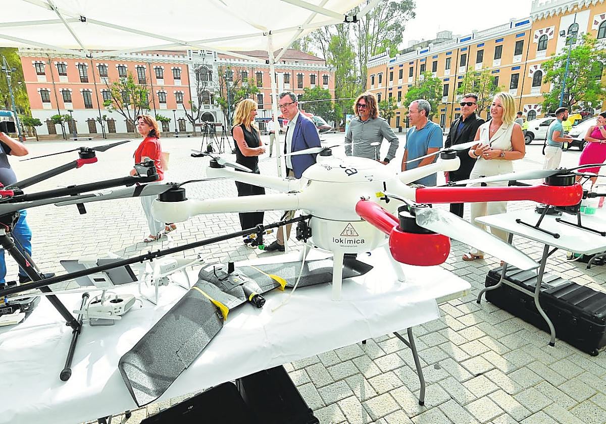 El alcalde Ballesta y la edil Torres observan algunos drones usados en el control de los mosquitos, con el helicóptero de fondo.