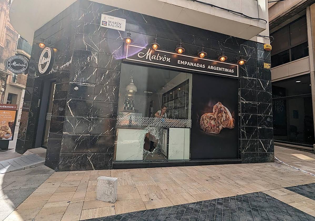 Agujero en el escaparate de empanadas Malvón por el que accedieron al interior del local para robar este jueves.