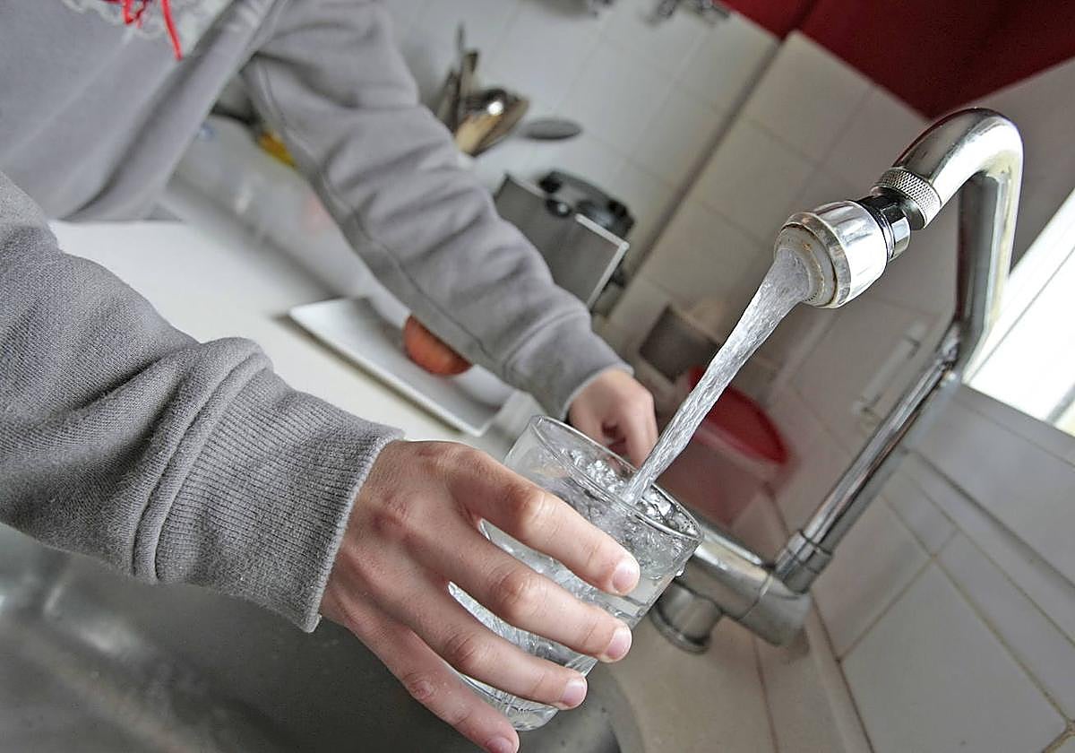 Una persona llena un vaso con un dispositivo para el ahorro de agua en casa