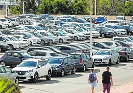 Dos personas caminan junto a un solar repleto de coches en el campus de la Muralla del Mar ayer por la mañana.
