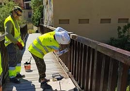 Dos alumnos pintando la pasarela del acceso desde la Vía Verde.