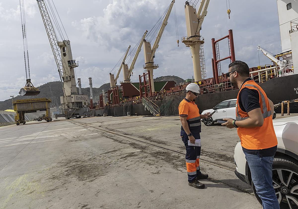 Dos trabajadores en los muelles de Escombreras, mientras otros descargan un barco de cereales.