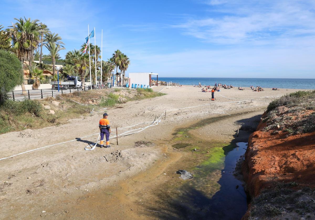 Operarios vuelven a balizar este martes el vertido sobre la arena de Cala Estaca. Al fondo, un grupo de bañistas disfruta del buen tiempo.