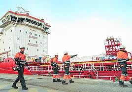 Cuatro operadores se disponen a descargar aceites usados del 'Med Arctic' en el muelle de Repsol.