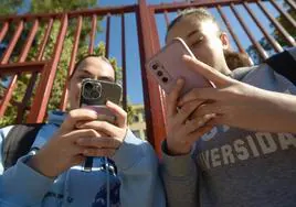 Dos alumnas consultan sus teléfonos a la salida de clase a las puertas del IES Floridablanca de Murcia, ayer.