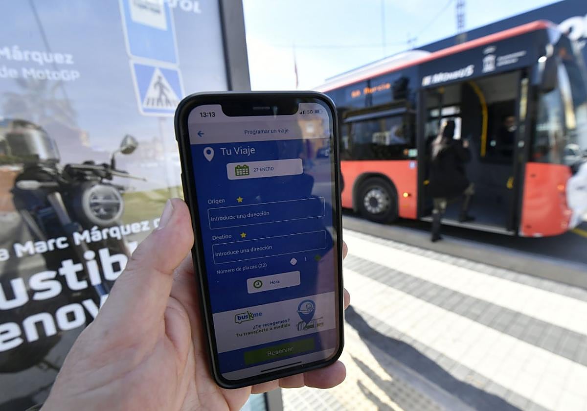 Un móvil muestra el modelo de aplicación usado en otras ciudades y que se empleará en Murcia, frente a un bus de Monbus.
