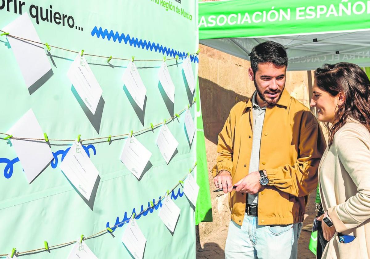 Miguel Ángel Ríos charla con la psicóloga de la Aecc Miriam Sánchez, ayer en la plaza de Santo Domingo, en Murcia, junto a un mural sobre loscuidados paliativos .