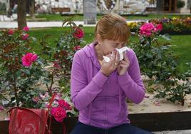 Una mujer se suena la nariz junto a varias flores.