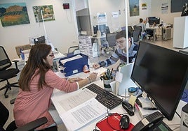 Una funcionaria atiende a un vecino en Torre Pacheco de forma manual, mientras el ordenador de su mesa permanece apagado.