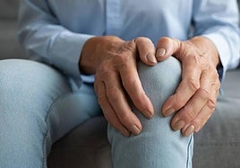 Una mujer se palpa la articulación de la rodilla por el dolor.