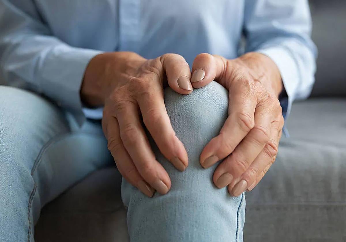 Una mujer se palpa la articulación de la rodilla por el dolor.