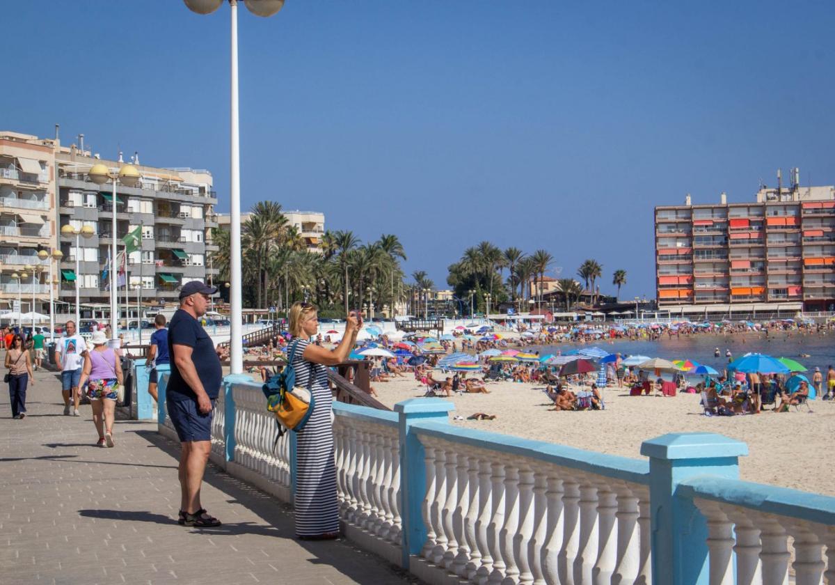 Unos turistas pasean junto a la playa de Los Locos.