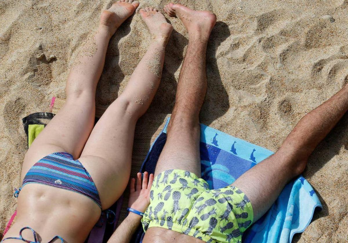 Dos personas con bañadores tomando el sol en la playa.