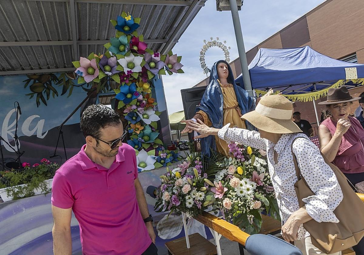 Una mujer toca la mano de la Dolorosa, con la cruz de mayo de fondo.
