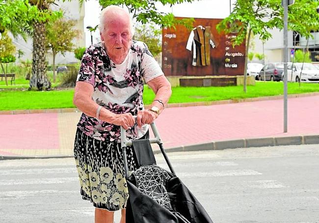 Carmen empuja un carro de la compra que le sirve de ayuda para caminar por Murcia.