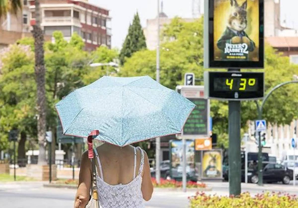 Una mujer pasea por Murcia y, al fondo, un termómetro marca 43 grados, en una imagen de archivo.