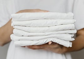 Una trabajadora de lavandería sostiene varios manteles recién doblados.