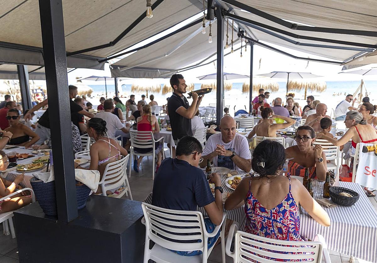 Un camarero con una paella de arroz lista para servir a los clientes de la terraza de un restaurante de La Manga.