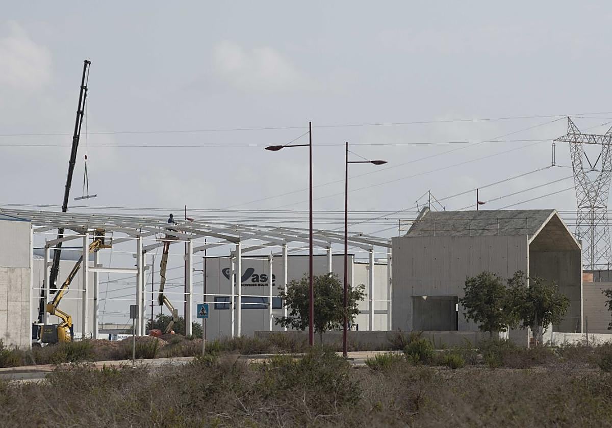 Un grupo de obreros con dos grúas trabajan en la construcción de una nave y del tanatorio.