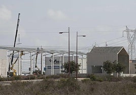 Un grupo de obreros con dos grúas trabajan en la construcción de una nave y del tanatorio.