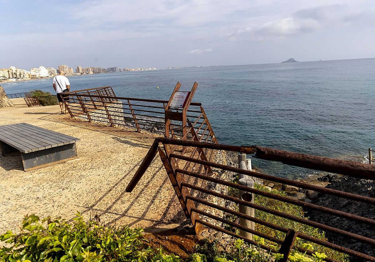 Un hombre se asoma al deteriorado mirador de la playa Galúa, con la barandilla rota y oxidada, en La Manga, este jueves.