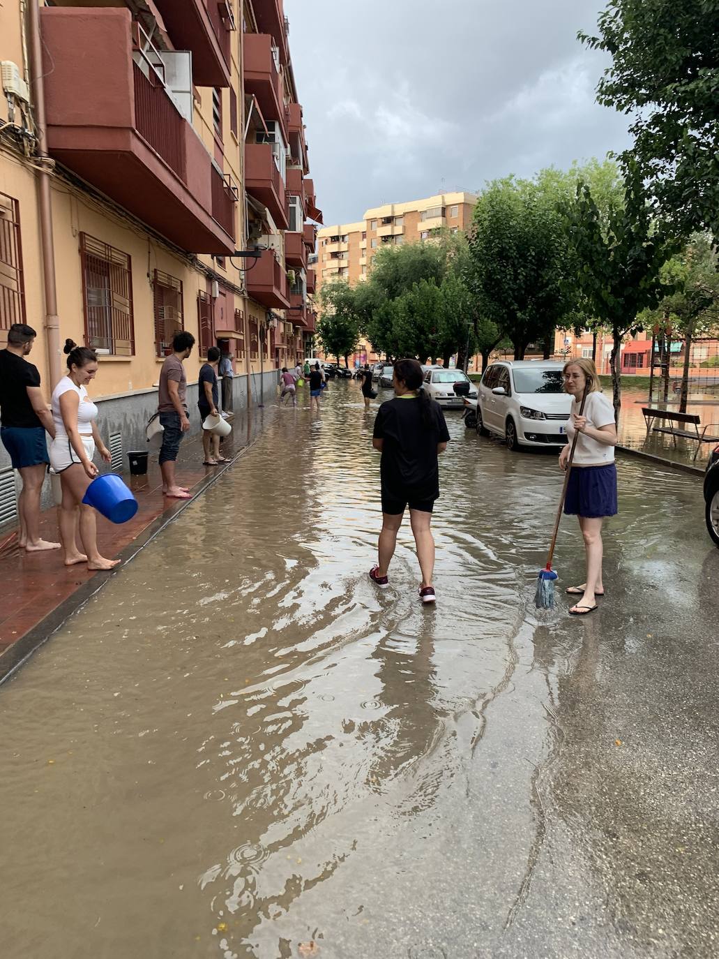 Los vecinos de la calle tratan de bajar el nivel de agua de la calle tras limpiar los imbornales el pasado 12 de junio tras las lluvias torrenciales.