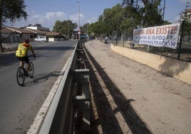 Un ciclista entra a Santa Ana, donde hay colocada una pancarta en la que los vecinos denuncian el «olvido de la administración».