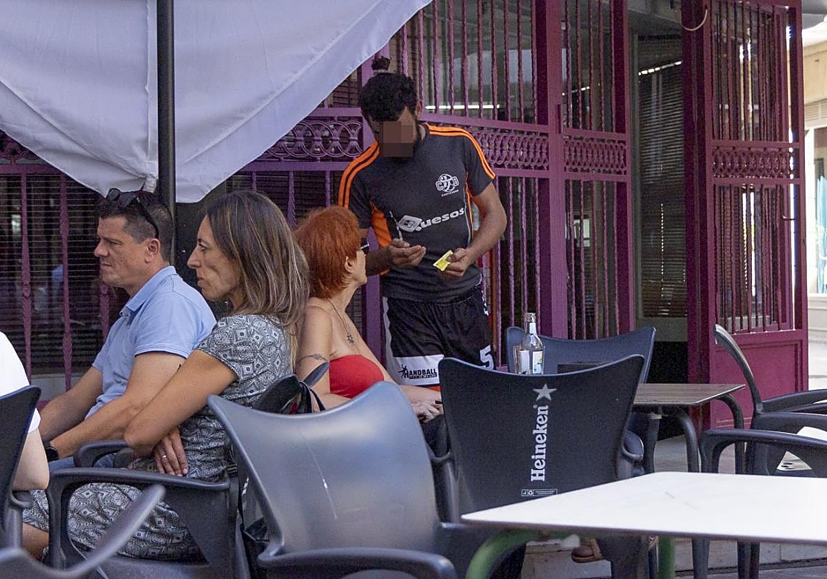 Un transeúnte pide una limosna a una mujer sentada en la terraza de un bar de la calle Honda.