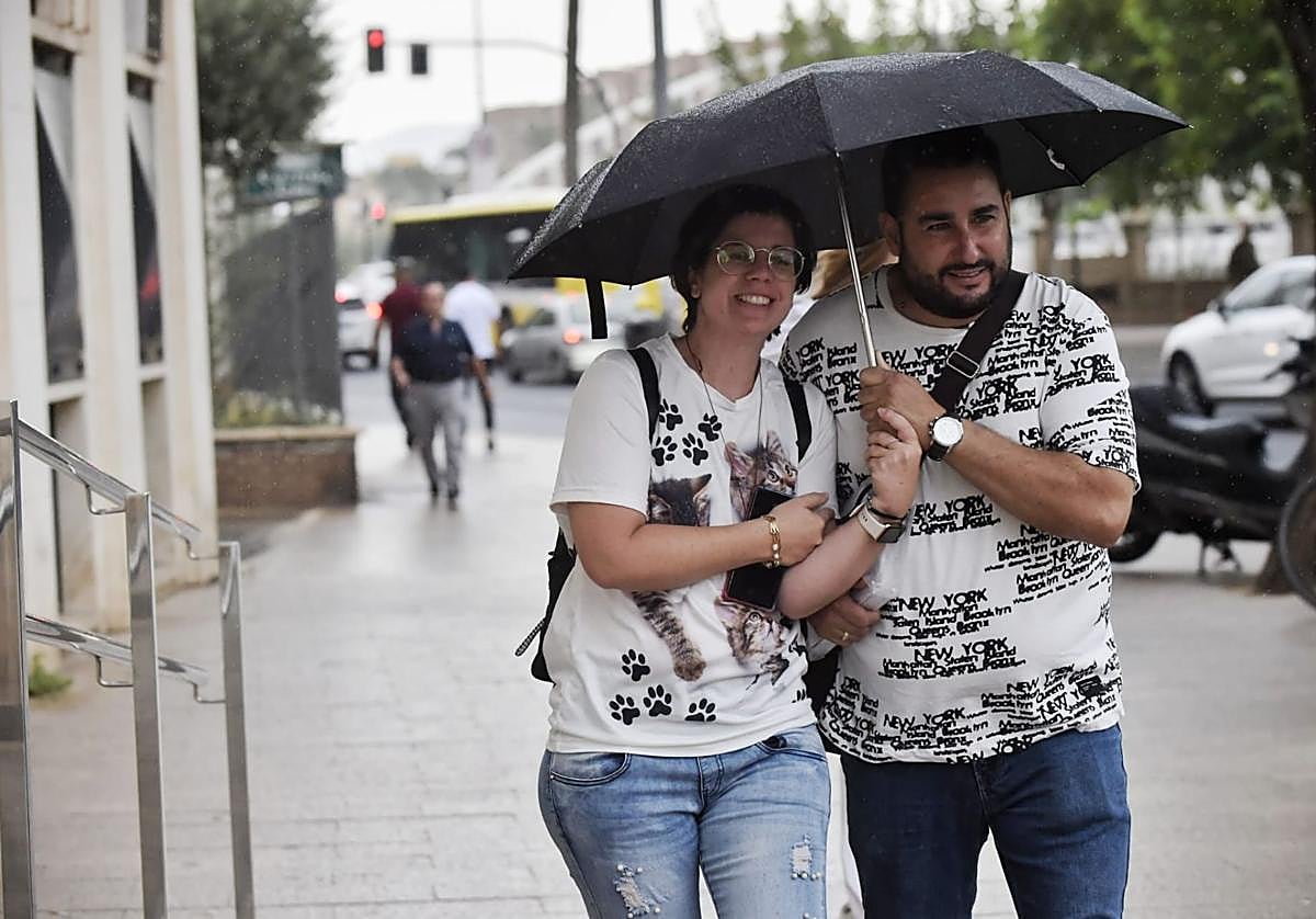 Un hombre y una mujer, este jueves en Murcia, resguardándose de la lluvia bajo un paraguas.