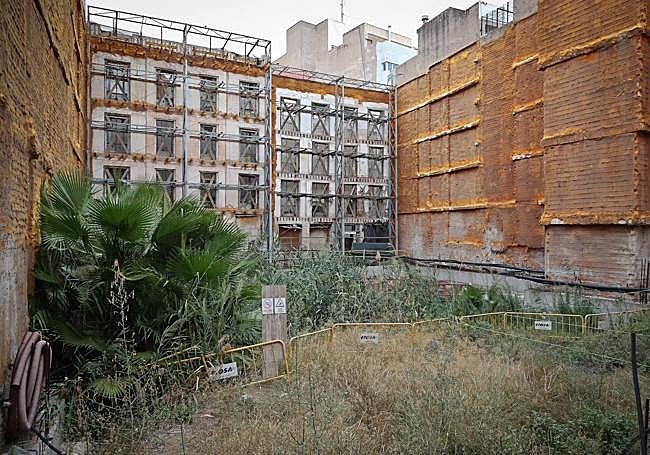 Vista trasera del edificio modernista, lleno de matorrales y restos de la obra.