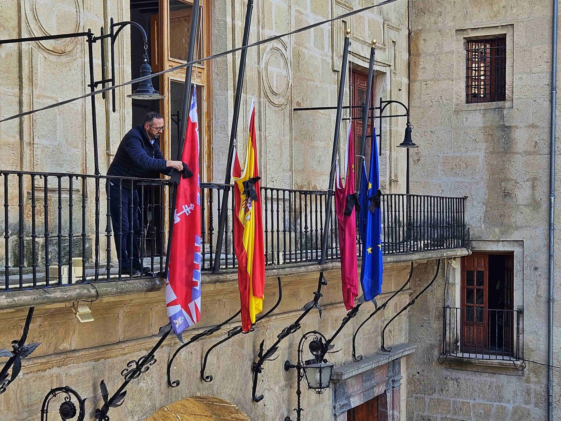 uUn funcionario municipal coloca crespones negros en las banderas del balcón principal del Ayuntamiento de Caravaca.