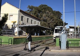 Un joven en patín cruza las vías del Feve en la estación de La Unión, mientras un automotor aguarda el momento de reiniciar la marcha.