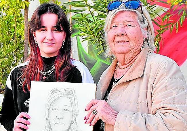 La estudiante de Bachillerato de Artes Plásticas Marta Sánchez y la residente Fina Martínez posan con la obra de grafito creada por la joven.