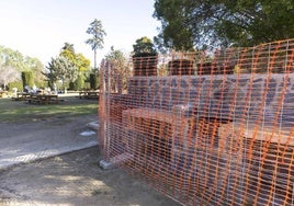 Varias familias disfrutan del sol en la zona de picnic del parque, cerca de una valla que delimita una zona en obras.