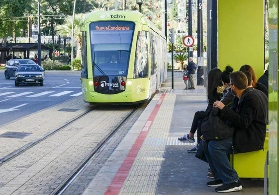 Varias personas esperan la llegada del tranvía de Murcia en una parada.