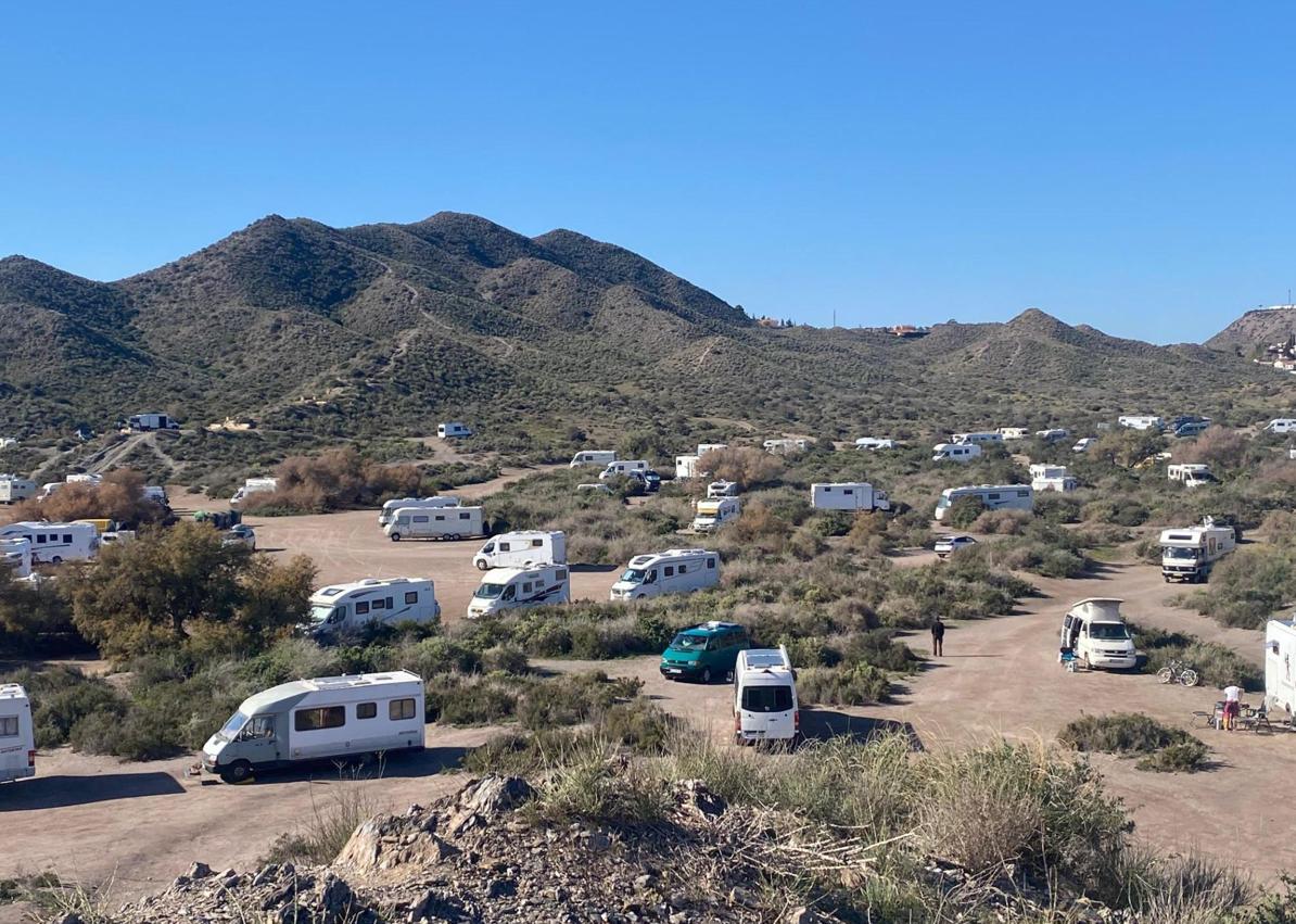 Imagen secundaria 1 - Autocaravanas instaladas al borde de la playa del Arroz y en sus inmediaciones, con elementos desplegados como sillas y tumbonas. El propietario de una autocaravana transporta un depósito del váter químico que acaba de vaciar junto al cartel de la playa del Arroz, que prohíbe expresamente acampar y aparcar.