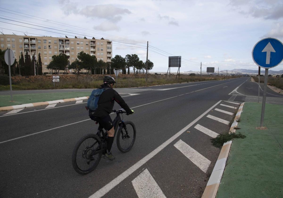 Un ciclista circula por la carretera N-332, a la altura del primero de los dos bloques de viviendas del residencial Buenos Aires; al fondo está Cartagena.