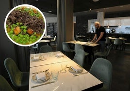 El personal de sala prepara una de las mesas en el comedor, con la cocina abierta al fondo.