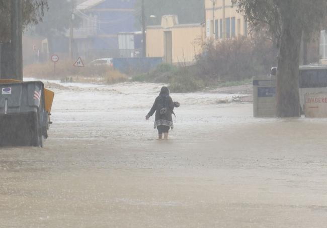 Una vecina de Lorca trata de cruzar una calle anegada de agua tras las lluvias de ayer por la tarde.