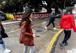 Estudiantes pasan frente a los acordonados ficus de la Muralla del Mar tratando de esquivar un charco en medio del adoquinado.