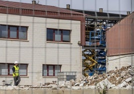 Dos obreros trabajan en el desmontaje y derribo del edificio de talleres portuarios.