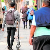 Un joven pasea por la calle Mayor de Alcantarilla mientras lleva un patinete con la mano.