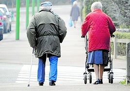 Una pareja de ancianos con problemas de movilidad camina por la calle.
